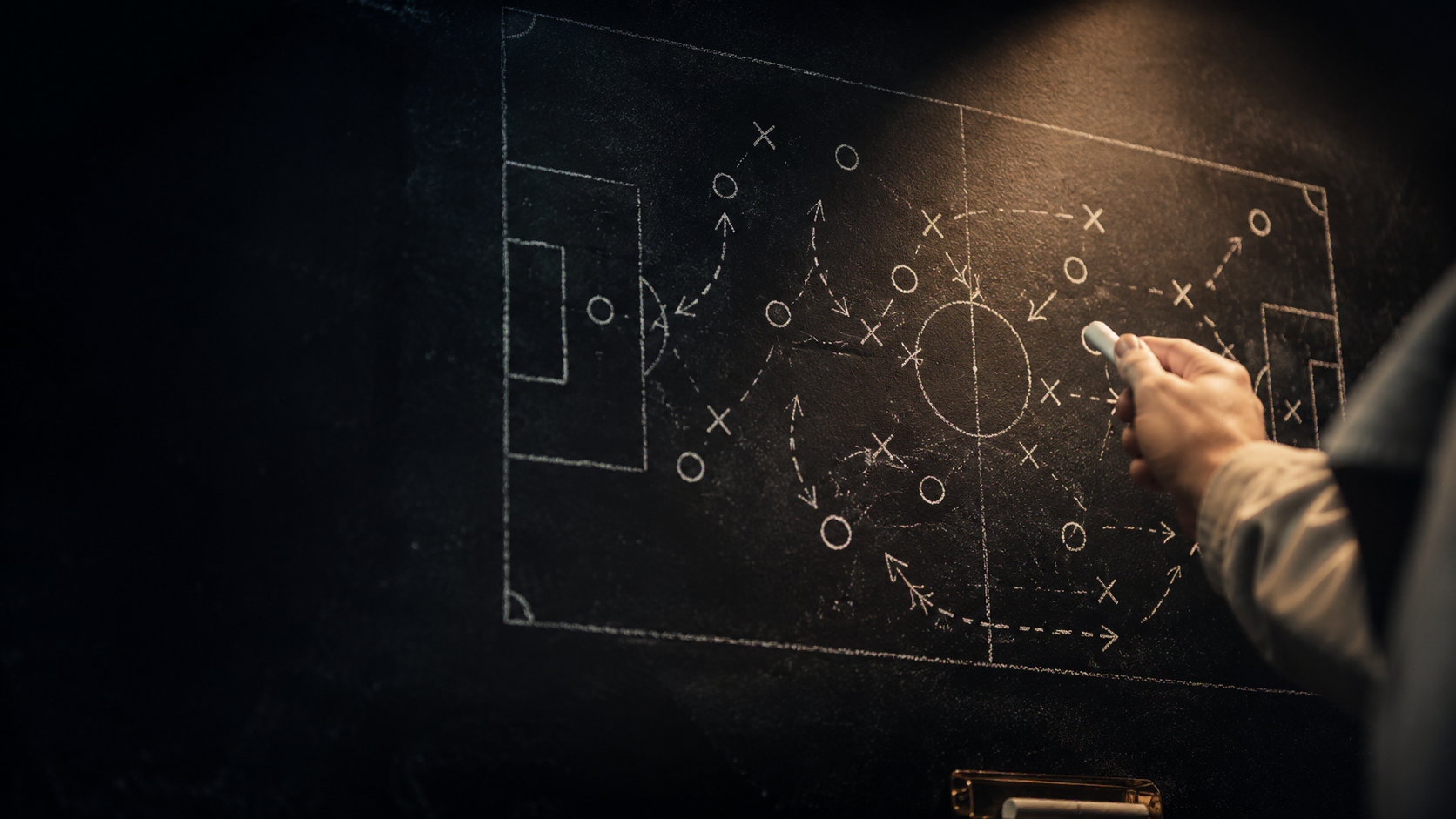 Tactical analysis board with chalk-drawn football formation and a manager's hand pointing at pressing triggers - elite coaching session