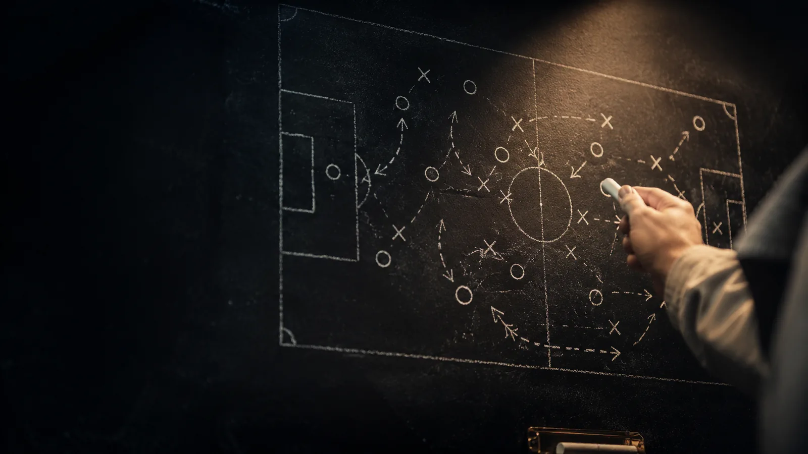 Tactical analysis board with chalk-drawn football formation and a manager's hand pointing at pressing triggers - elite coaching session
